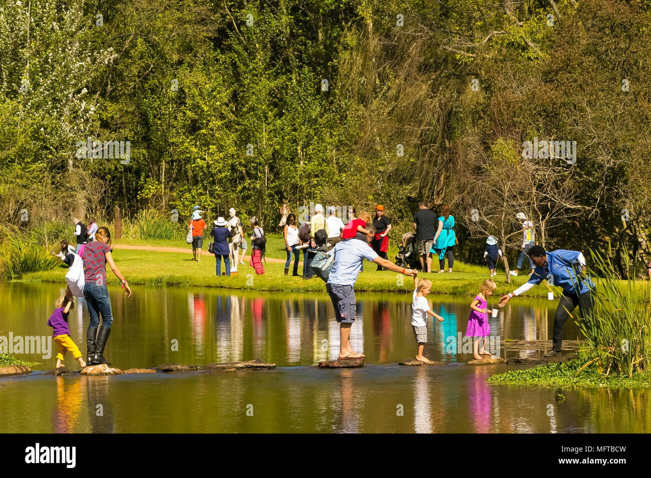 Johannesburg, Sud Africa, 05/10/2014, Famiglia attraversare un torrente su pietre miliari all'Inverno scultura fiera a Nirox Sculpture Park Foto Stock