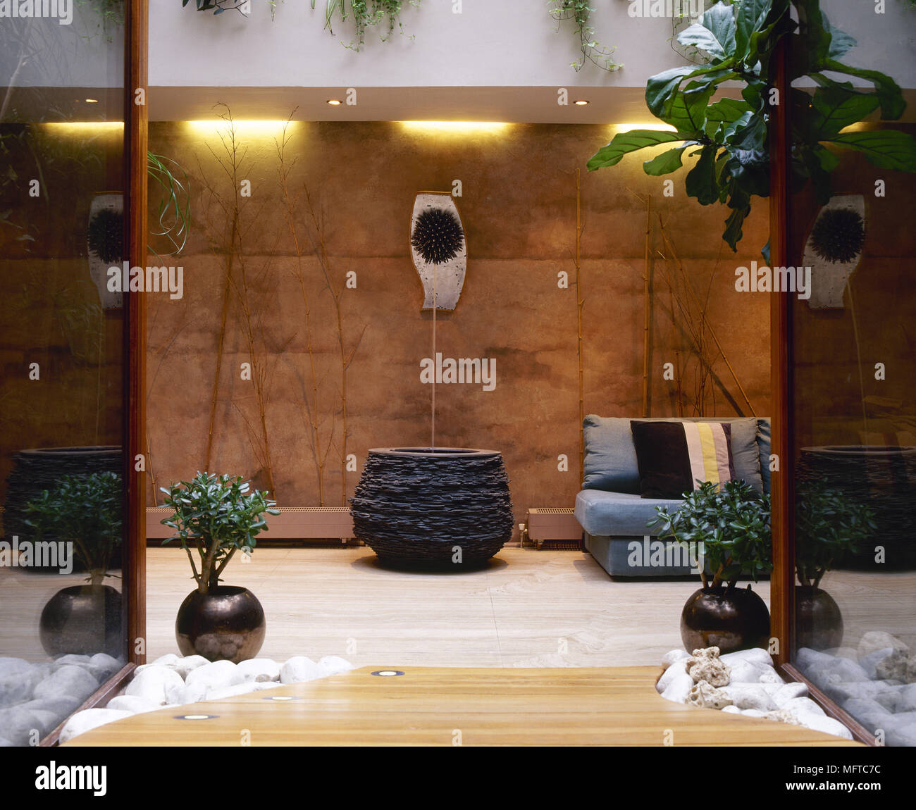 Contemporary salotto con divano, pietra e pareti di vetro, acqua caratteristica e di piante in vaso. Foto Stock
