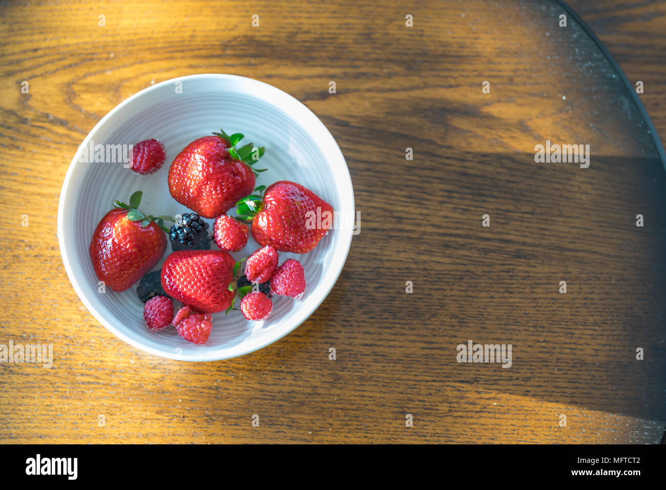 Fragole, lamponi e more flottante in una tazza di acqua Foto Stock