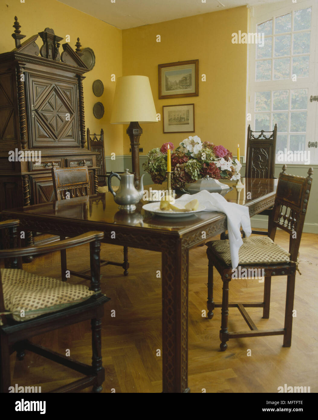 Tradizionale sala da pranzo giallo e verde pallido pareti tavolo sedie cuscini ornati scolpiti unità laterali interni camere standard colore lampada abat-jour fram Foto Stock