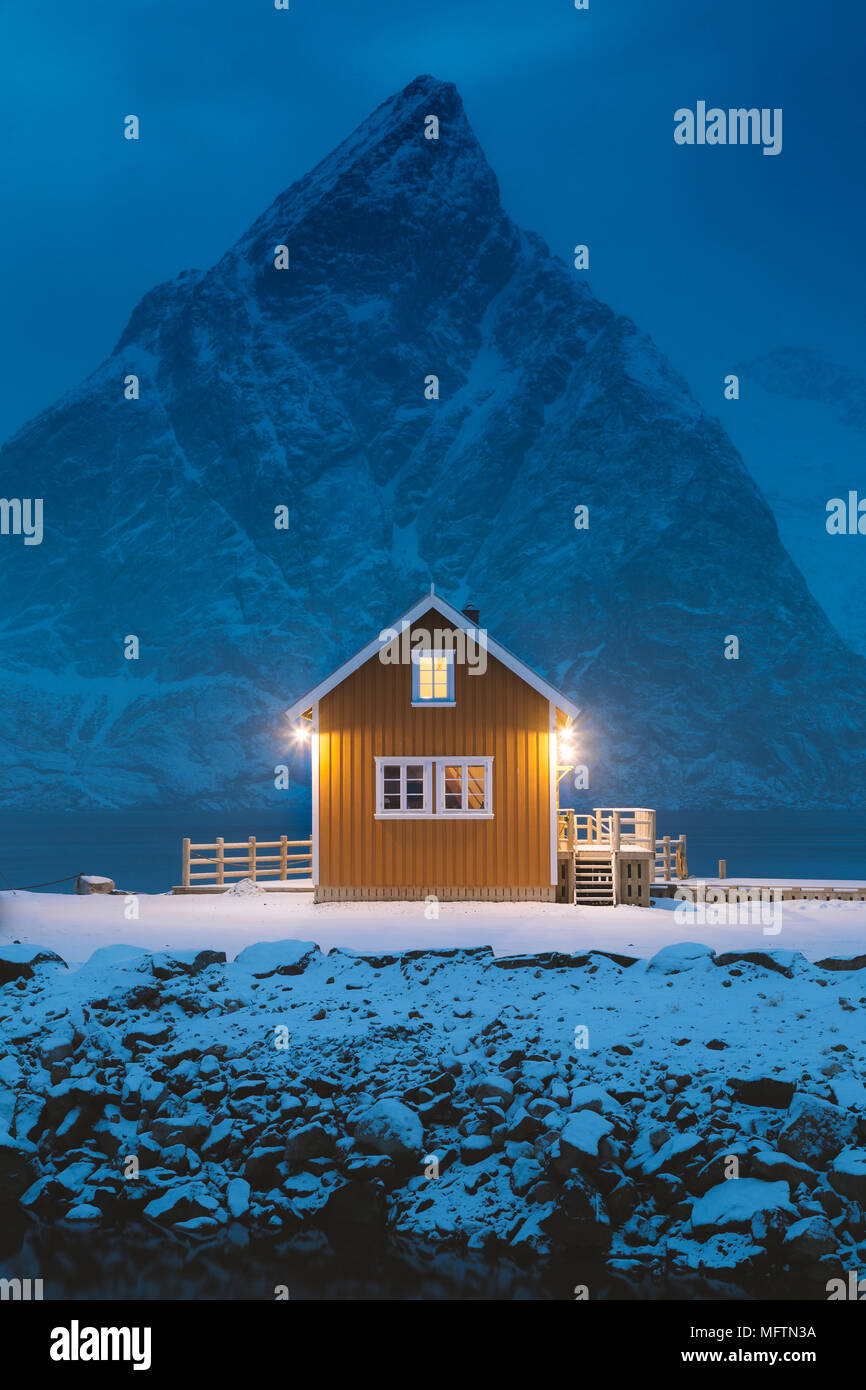 Tradizionale giallo Rorbu cabina con Olstinden picco di montagna al crepuscolo in inverno, villaggio di Sakrisoy nei, Isole Lofoten arcipelago, Norvegia Foto Stock