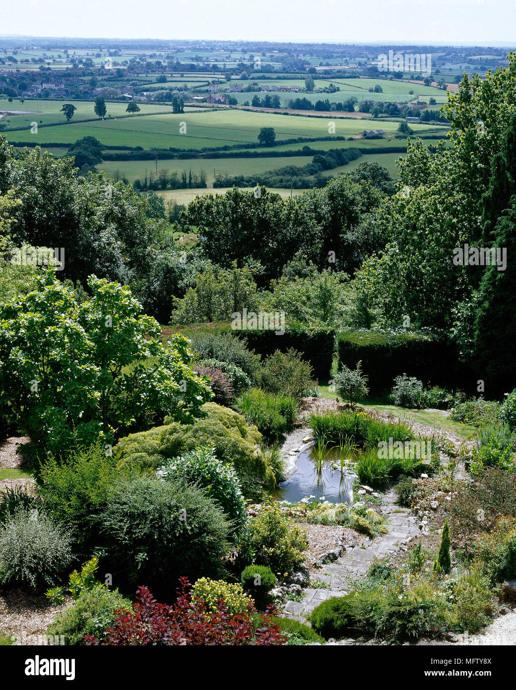 Un paese giardino con laghetto e rockery con vista della campagna circostante, Foto Stock