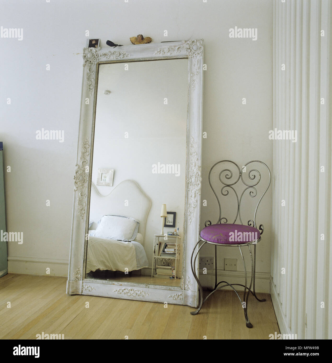 Un dettaglio di una moderna camera da letto specchio oversize appoggiata contro il muro di ferro battuto sedia con sedile viola pianale in legno Foto Stock