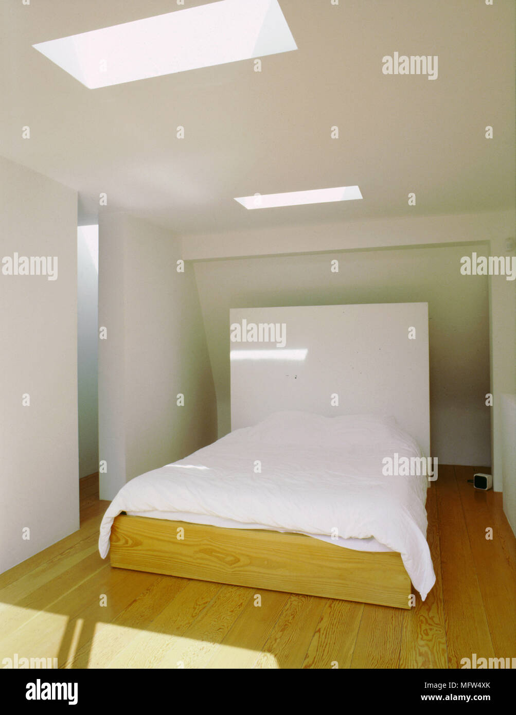 Moderna camera da letto in stile minimalista con pavimenti in legno letto a piattaforma con testiera bianco e una coppia di lucernari. Foto Stock