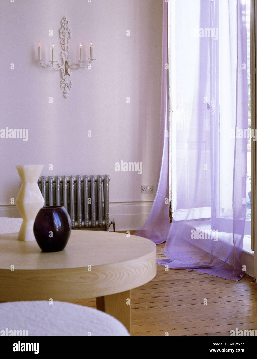 Moderno salotto dettaglio con pavimento di legno tondo tavolo in legno e viola e tende a strapiombo su aprire porte francesi. Foto Stock