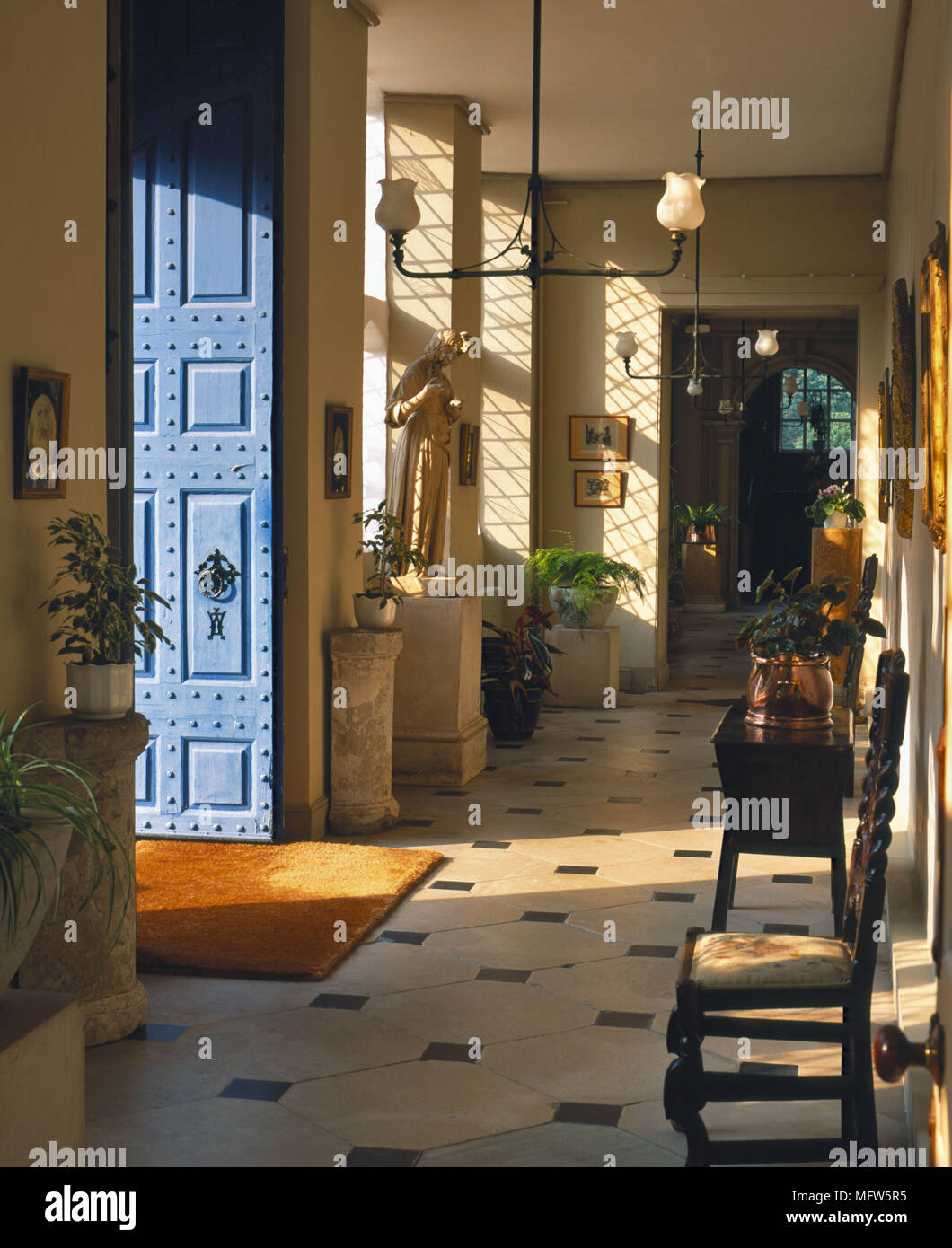 Un tradizionale corridoio al ingresso pavimento piastrellato con porta aperta in stile giacobino sedia in legno Piante da interni Foto Stock