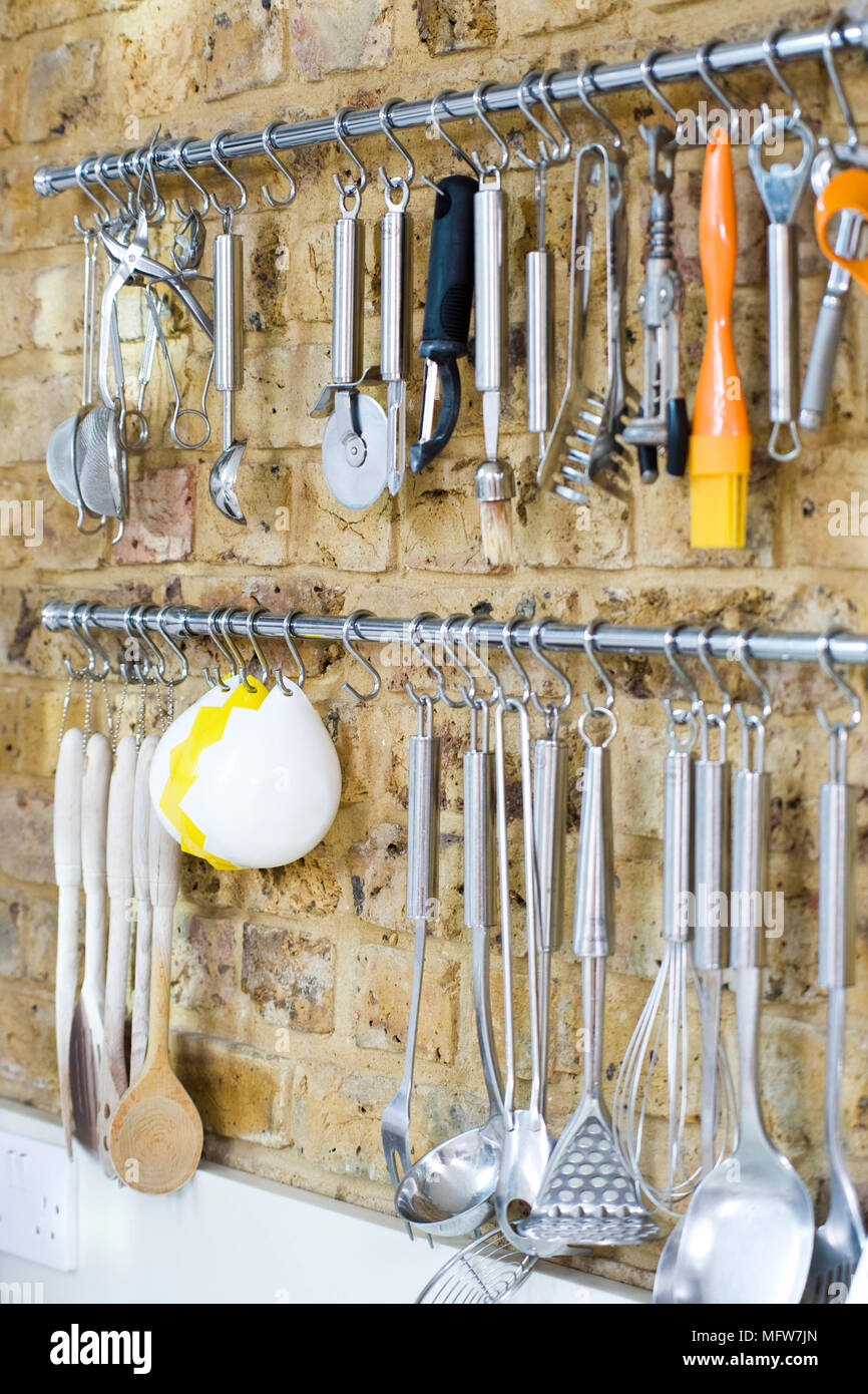 Varietà di utensili da cucina su rack pendenti contro un muro di mattoni di cucina Foto Stock
