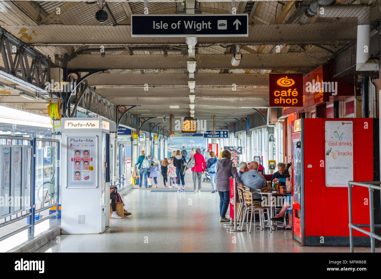 Una vista lungo un corridoio che gira a fianco di piattaforme in Portsmouth Porto Stazione ferroviaria. Le persone sono seduti in un caffè vicino a Photo Booth. Foto Stock