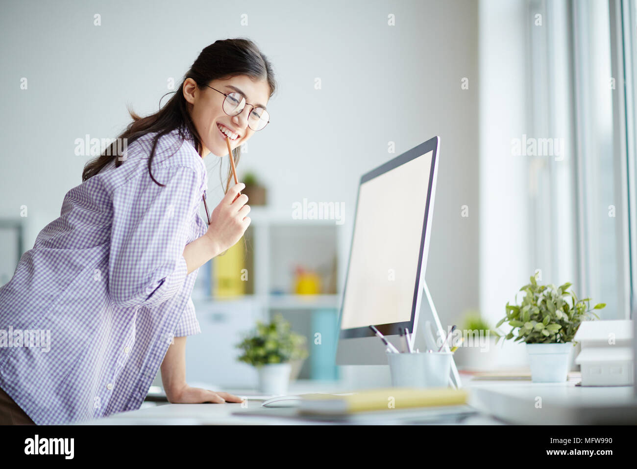 Ritratto di successo della giovane designer in piedi nella parte anteriore del computer e sorridente Foto Stock
