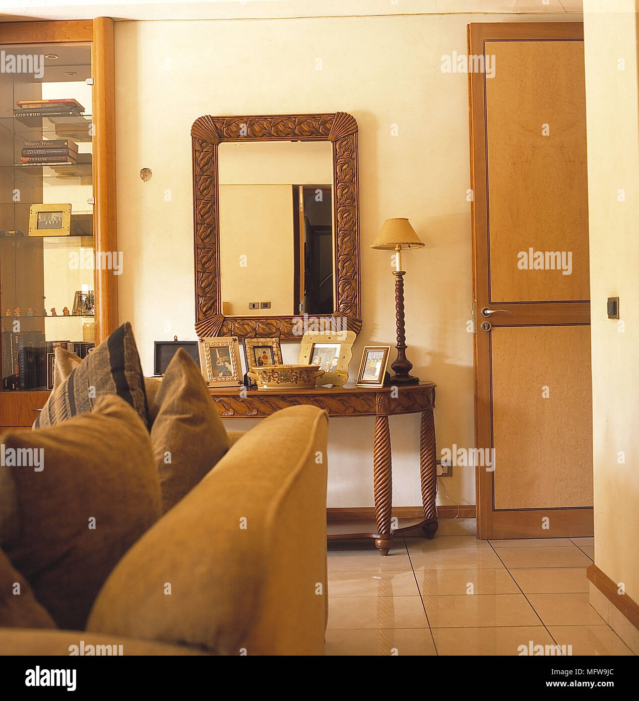 La stanza di seduta dettaglio pareti bianche pavimento piastrellato oro divano cuscini specchio lato intagliato lampada da tavolo interni camere vetro unità display libri fotografie p Foto Stock
