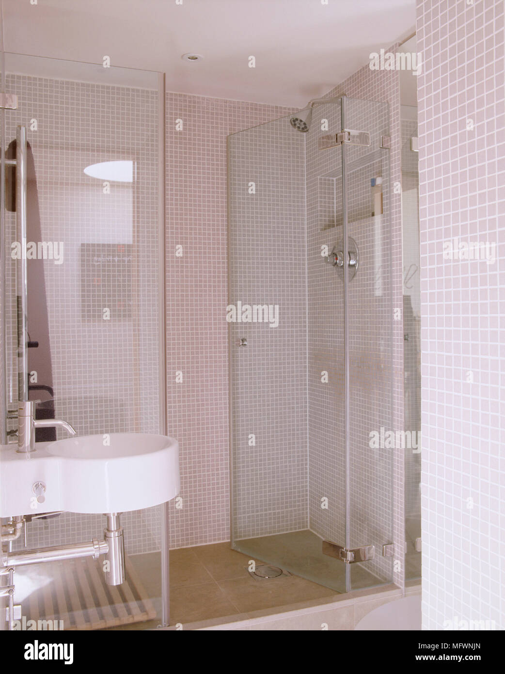 Un dettaglio di un moderno bagno neutro con mosaici di pareti piastrellate, un box doccia con porta in vetro e montato a parete lavabo Foto Stock