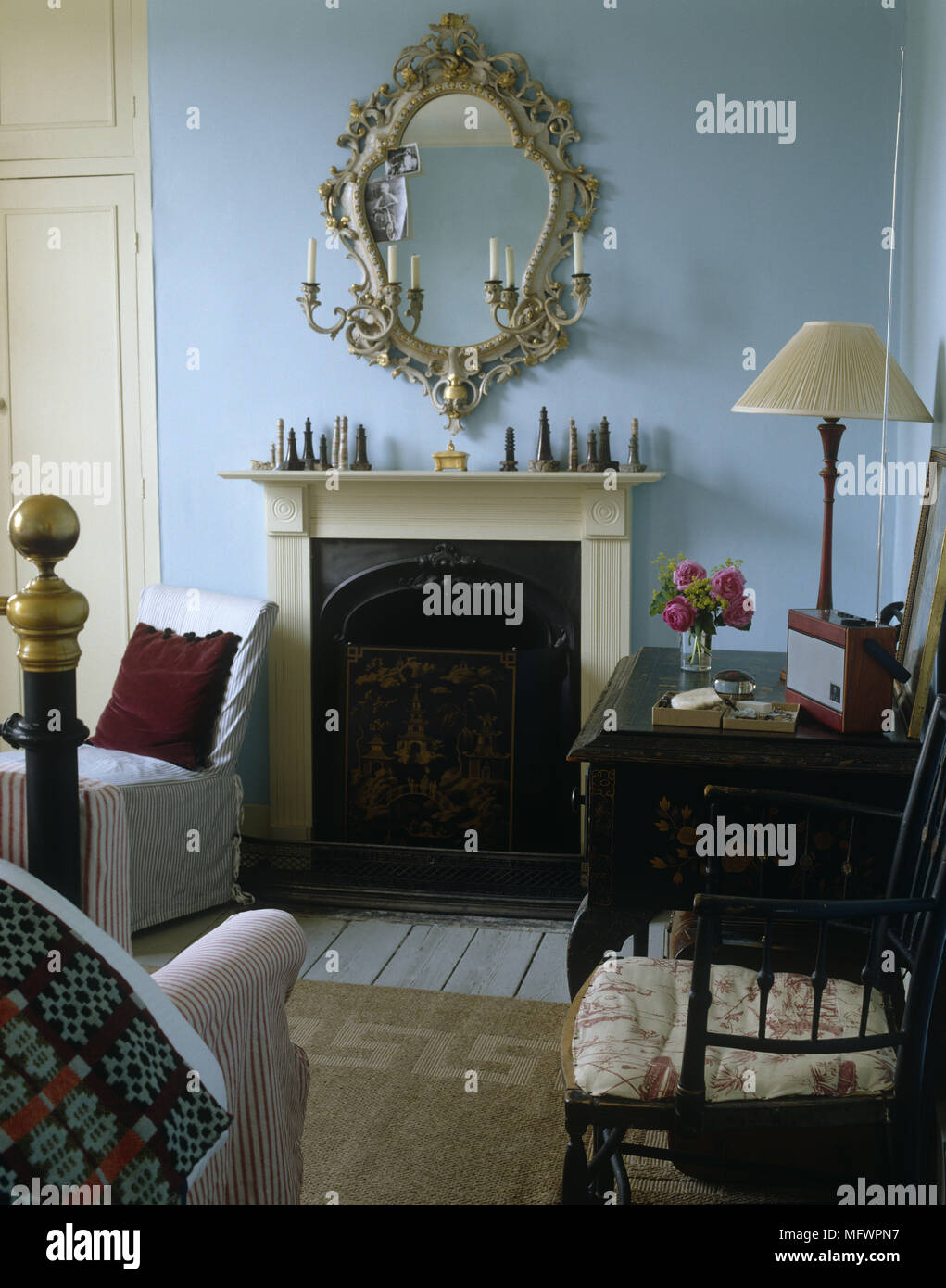 Specchio con cornice ornata al di sopra di camino vittoriano accanto al tavolo vestito e rivolta verso il telaio di ottone del letto Foto Stock