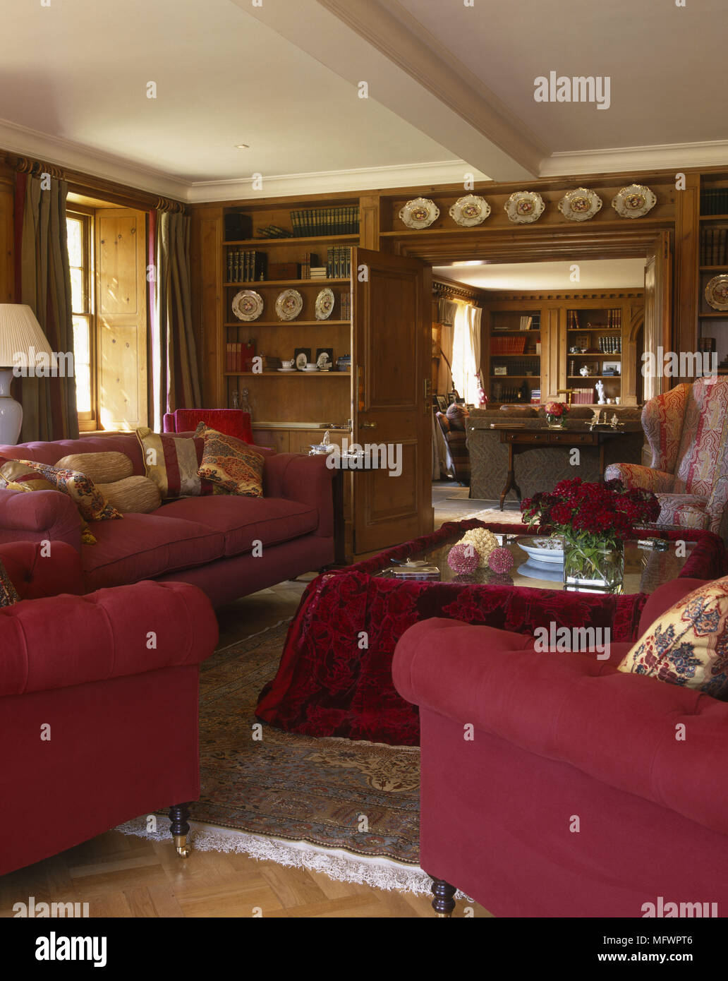 Salotto con divani rossi e sedie rivolta verso il tavolino con rivestimento in tessuto in camera con muri con pannelli in legno Foto Stock