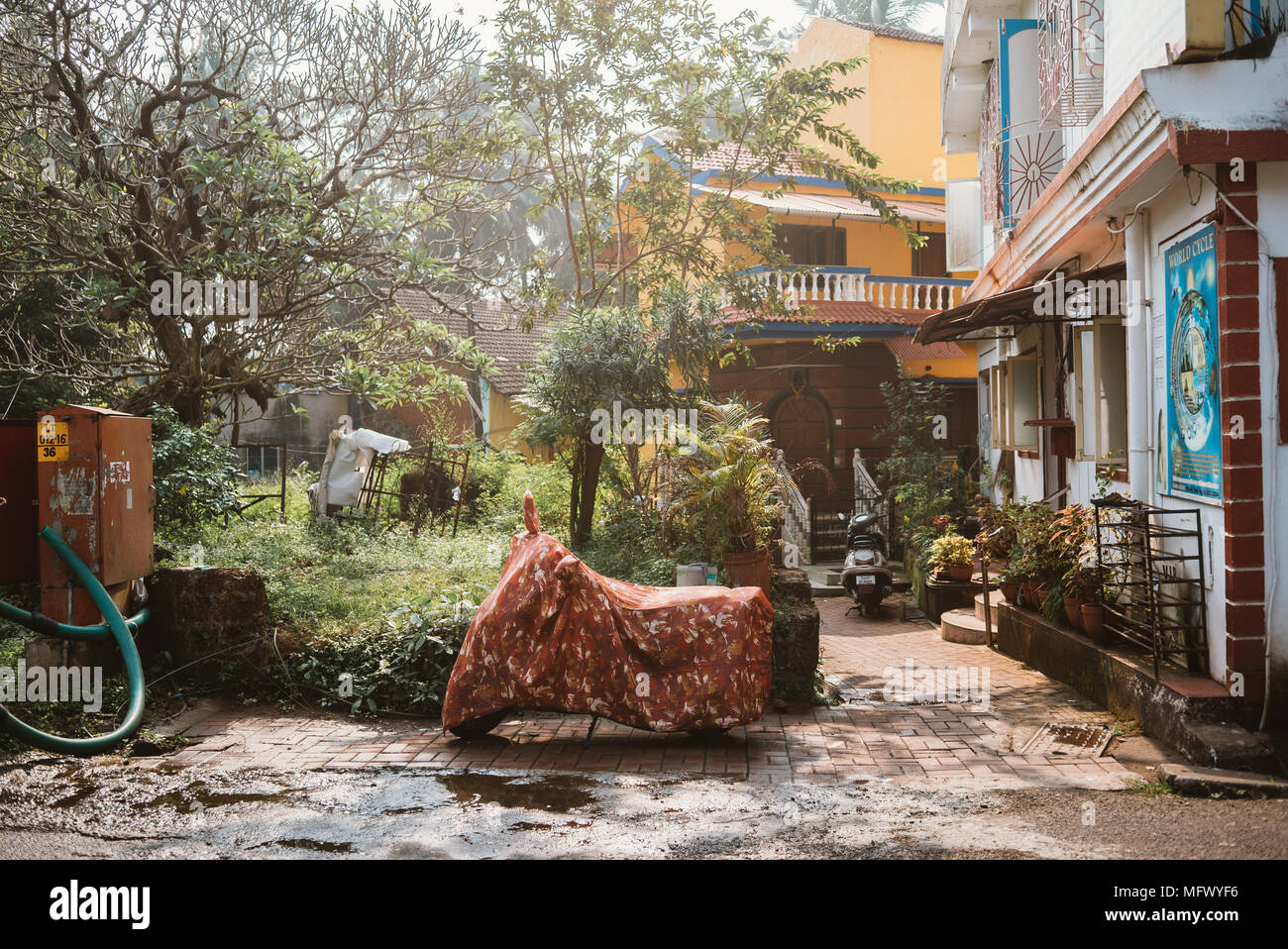 Motocicletta con coperchio floreale il parcheggio nel cortile di casa in Goa, India Foto Stock