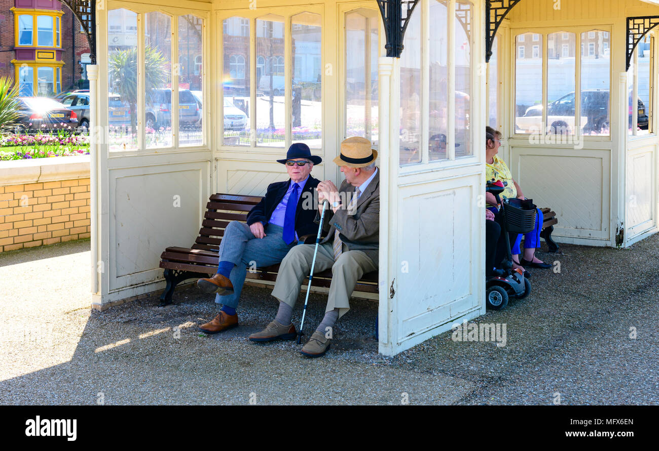 Due anziani signori avente una chat in un rifugio sul lungomare, Herne Bay Kent Foto Stock