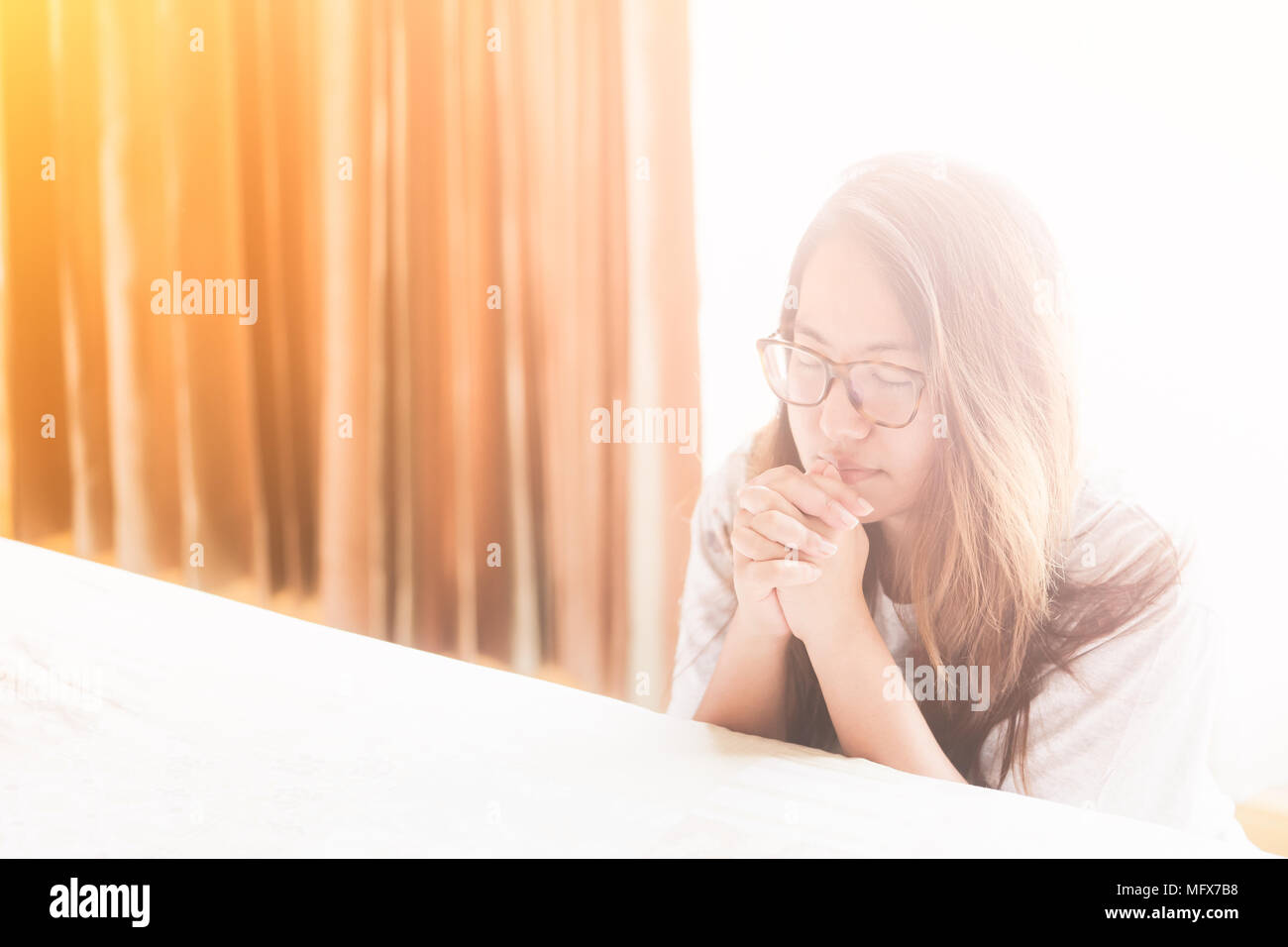 Donna orante sul letto la mattina.adolescente donna orante a mano,mani giunte in preghiera sul letto la mattina concetto per la fede e la spiritualità di un Foto Stock
