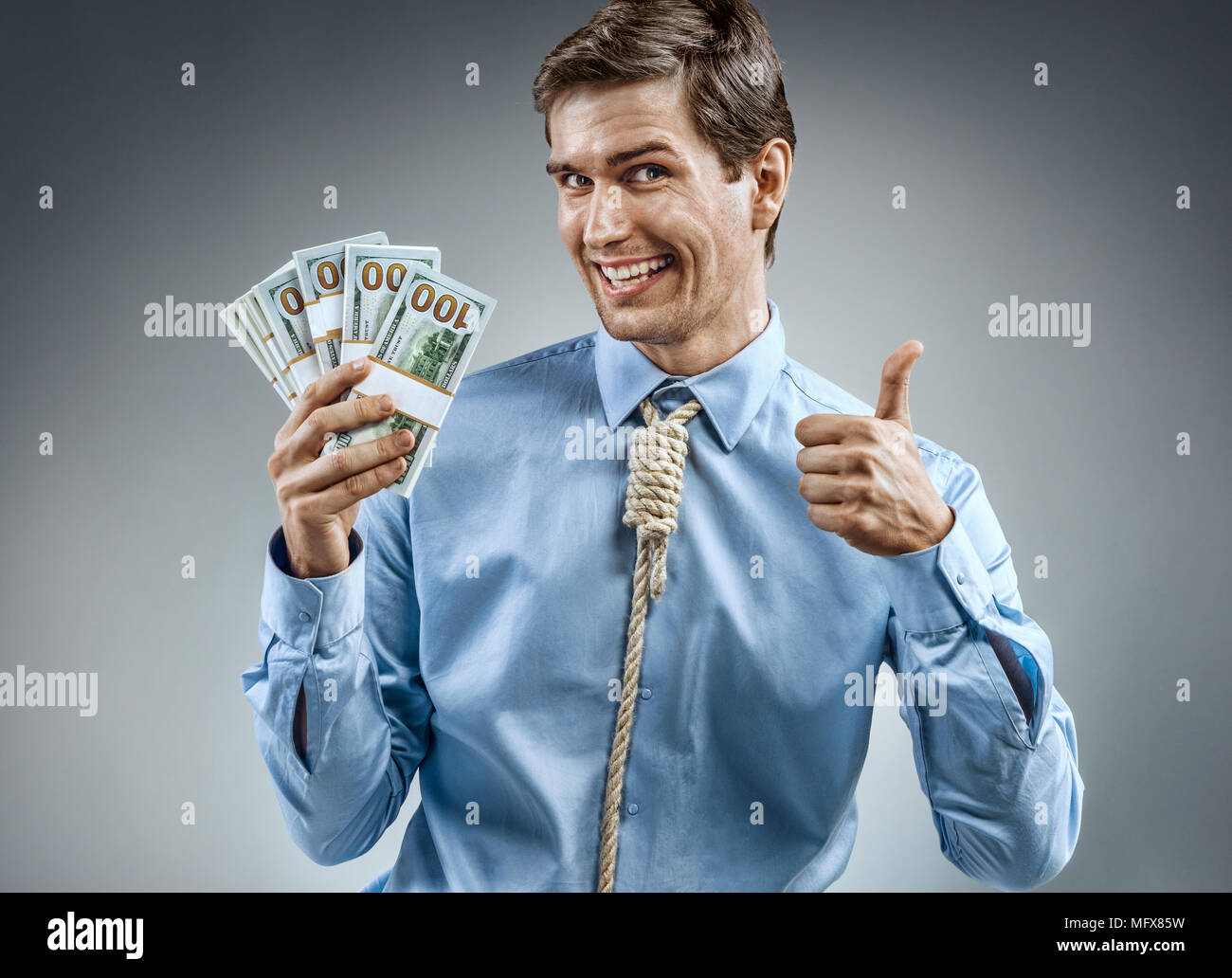 Uomo con denaro contante e mostrando il pollice verso l'alto. Foto di uomo sorridente in maglietta blu e cravatta in forma di ansa sul suo collo su sfondo grigio Foto Stock
