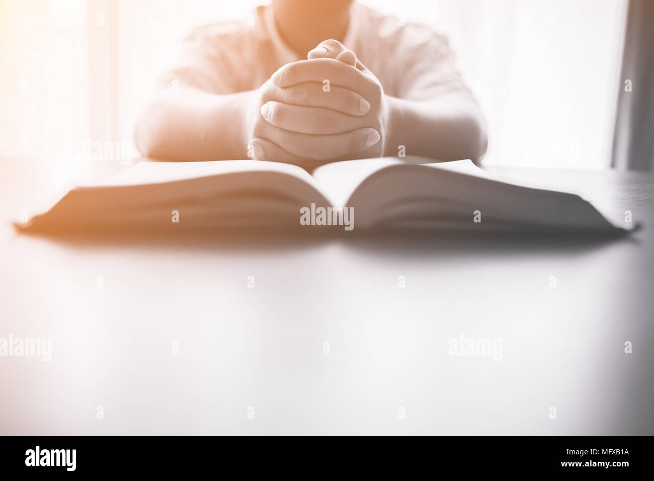 Uomo che prega sulla Sacra Bibbia in mattinata.ragazzo adolescente mano con la Bibbia pregando,mani giunte in preghiera in una Sacra Bibbia nel concetto di chiesa per la fede, spir Foto Stock