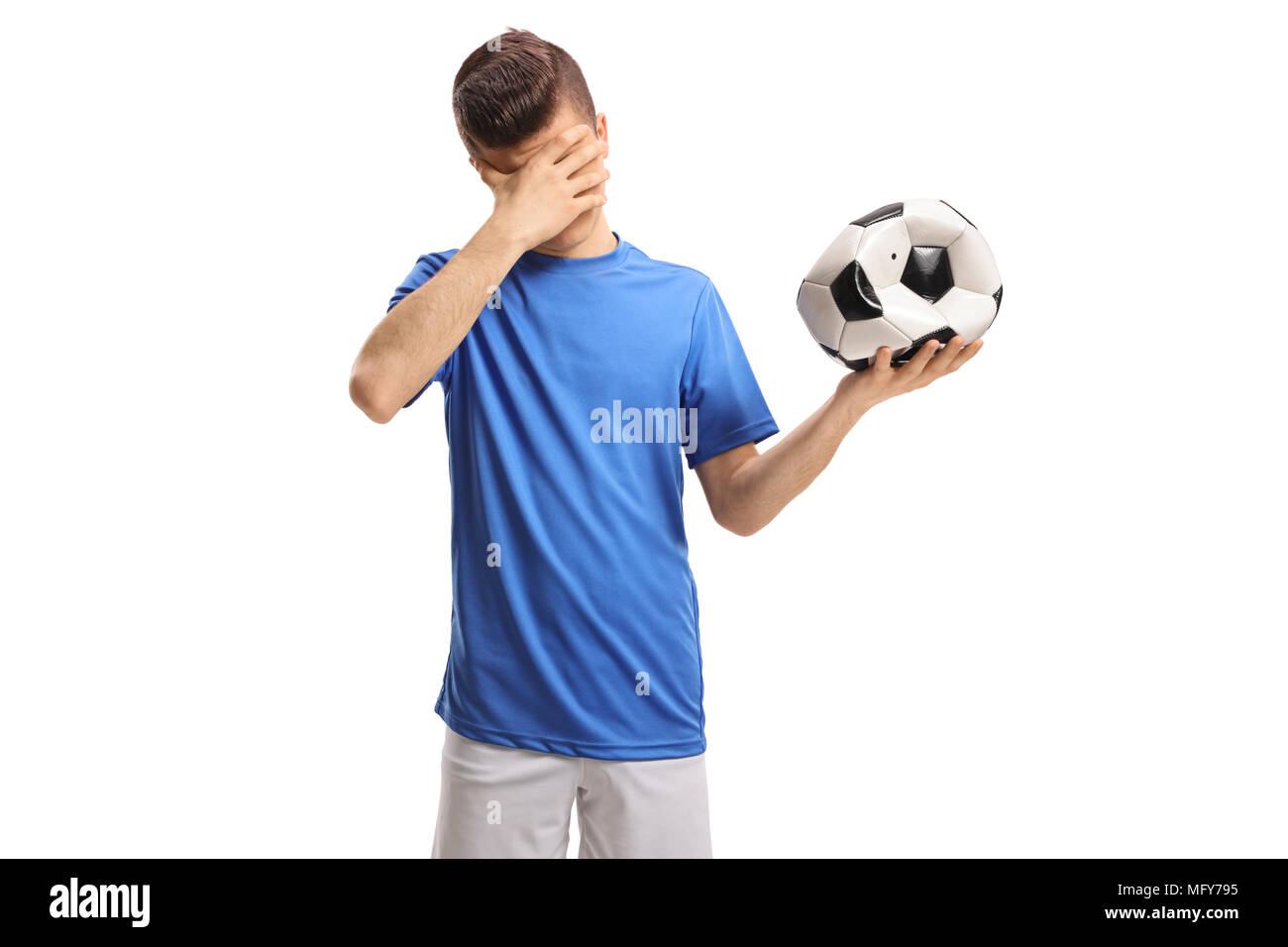 Teenage giocatore di calcio con un calcio sgonfio tenendo la sua testa in incredulità isolati su sfondo bianco Foto Stock