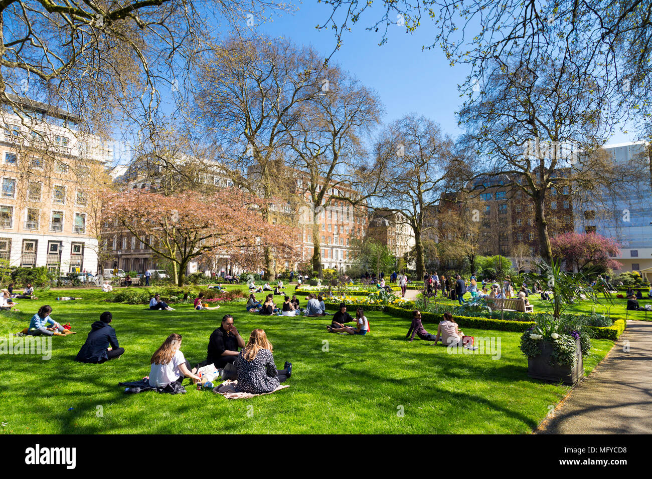 La Gente seduta sul prato e mangiare il pranzo in un piccolo parco cittadino, St James's Square Garden, Londra, Regno Unito Foto Stock