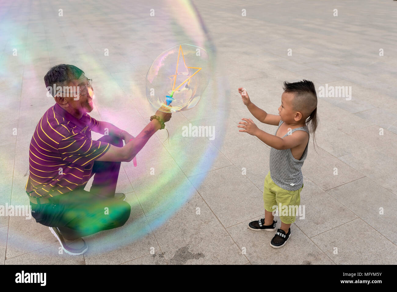 Nonno crea bolle giganti per la nipote durante la riproduzione in city square, Xilinhot, Mongolia Interna, Cina Foto Stock