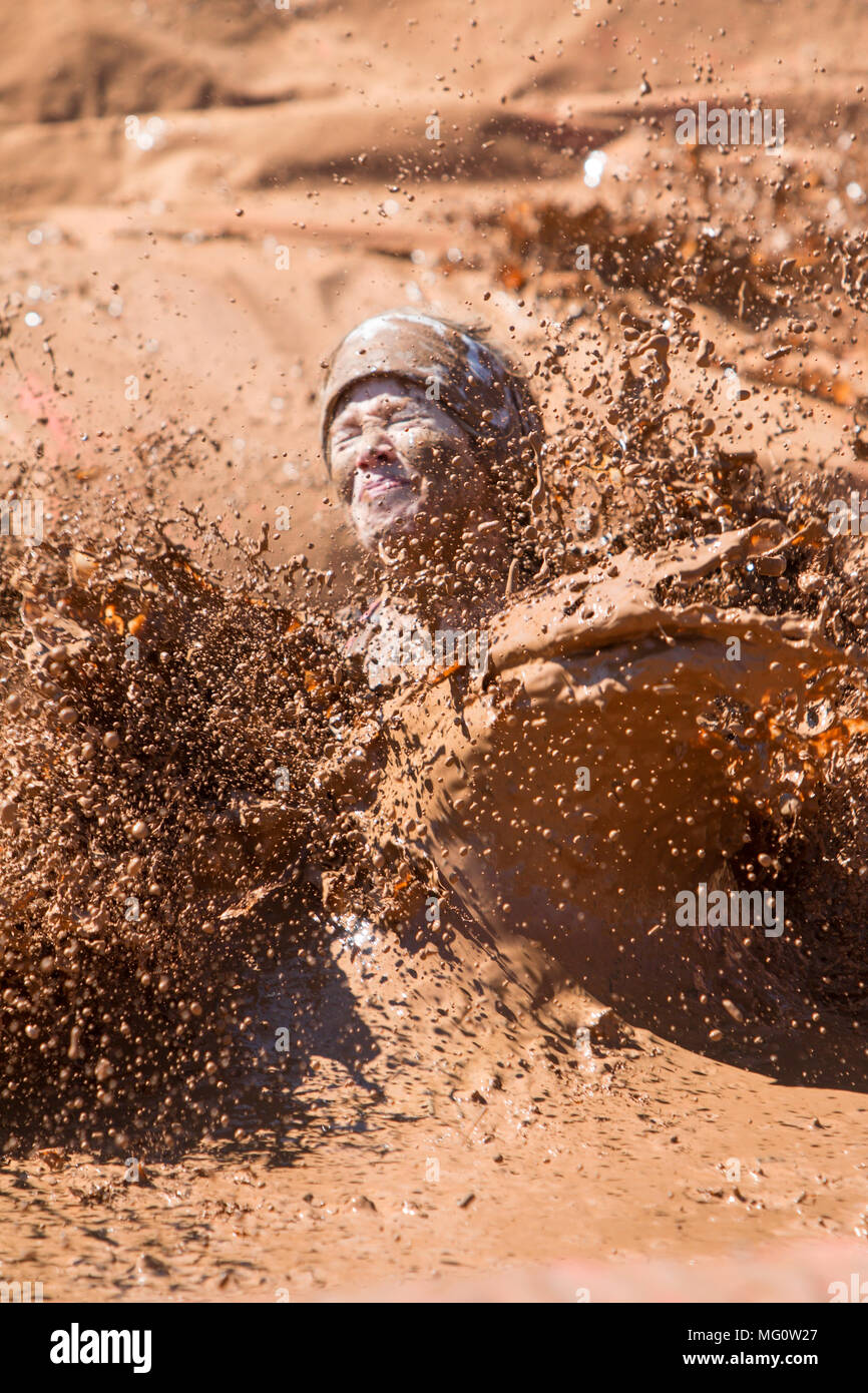 Una donna crea un grande splash di acqua fangosa come lei atterra in un pozzo del fango alla ragazza sporca di fango eseguire ostacolo corso evento su Aprile 23, 2016 in Hampton, GA. Foto Stock