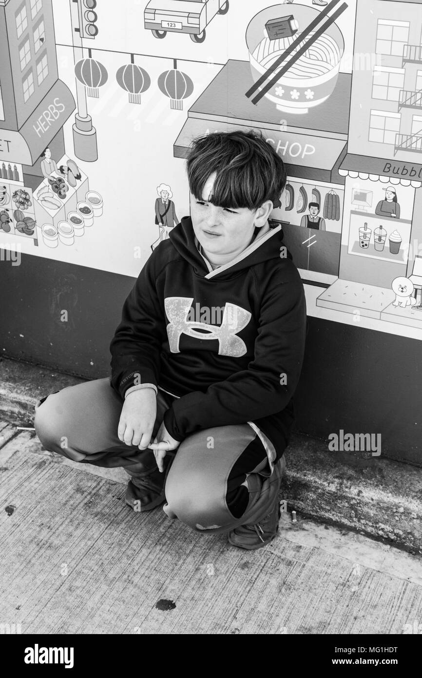 Giovane ragazzo accovacciato su strada Foto Stock