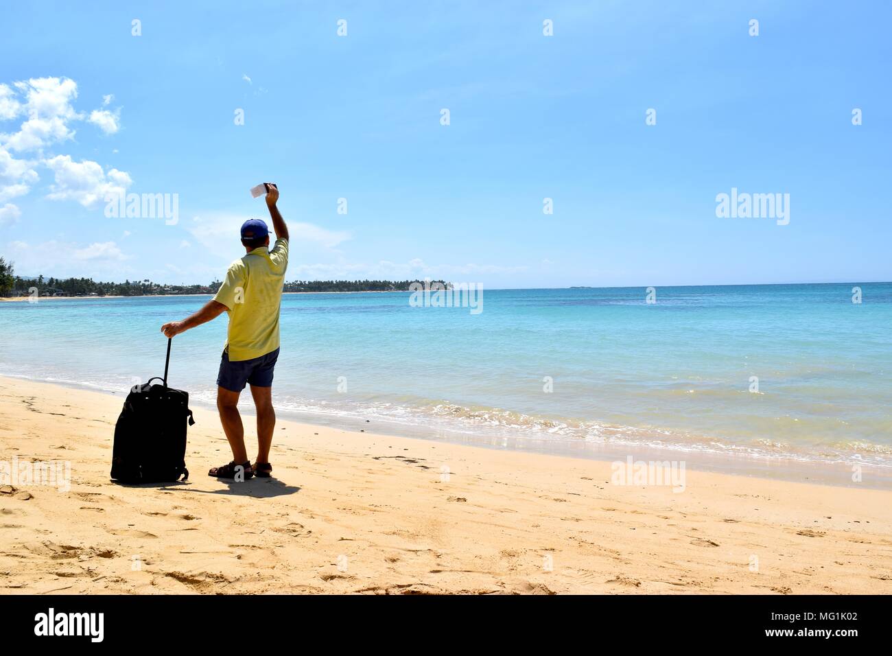 Un uomo di mezza età su di una spiaggia di sabbia in possesso di una valigia e un biglietto nelle sue mani. Foto Stock