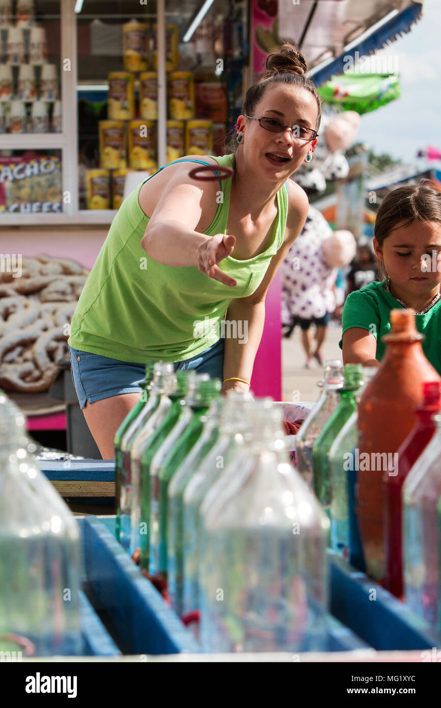 Una giovane donna di lanci un anello a bottiglie di vetro nell'anello toss gioco al Gwinnett County Fair, il 17 settembre 2016 in Lawrenceville, GA. Foto Stock
