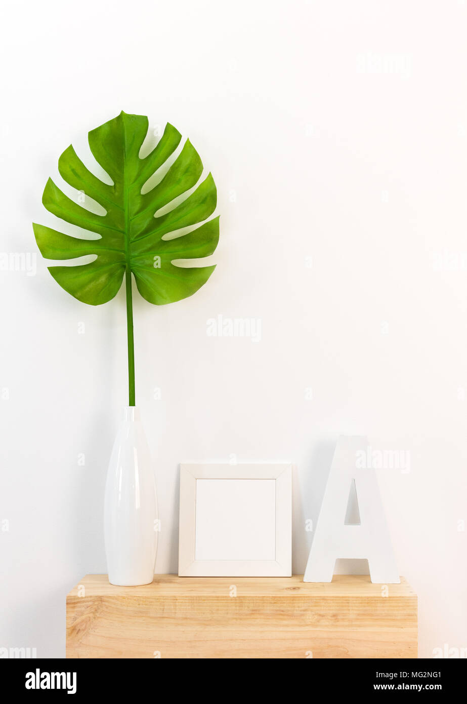 Elegante arredo della casa bianca con cornice immagine, verde foglia tropicale in un vaso e una lettera su una superficie di legno. Foto Stock
