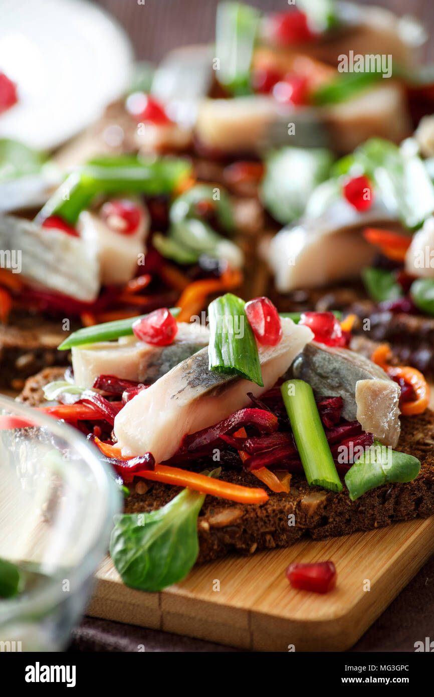 La bruschetta su pane di segale con cannucce fritto di barbabietole e carote, verdi e fette di aringa su una scheda di bambù. Messa a fuoco selettiva. Foto Stock