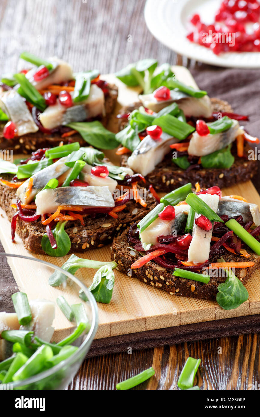 La bruschetta su pane di segale con cannucce fritto di barbabietole e carote, verdi e fette di aringa su una scheda di bambù. Messa a fuoco selettiva. Foto Stock