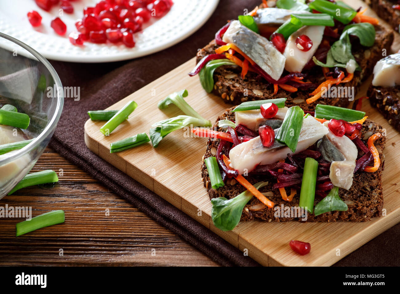 La bruschetta su pane di segale con cannucce fritto di barbabietole e carote, verdi e fette di aringa su una scheda di bambù. Messa a fuoco selettiva. Foto Stock