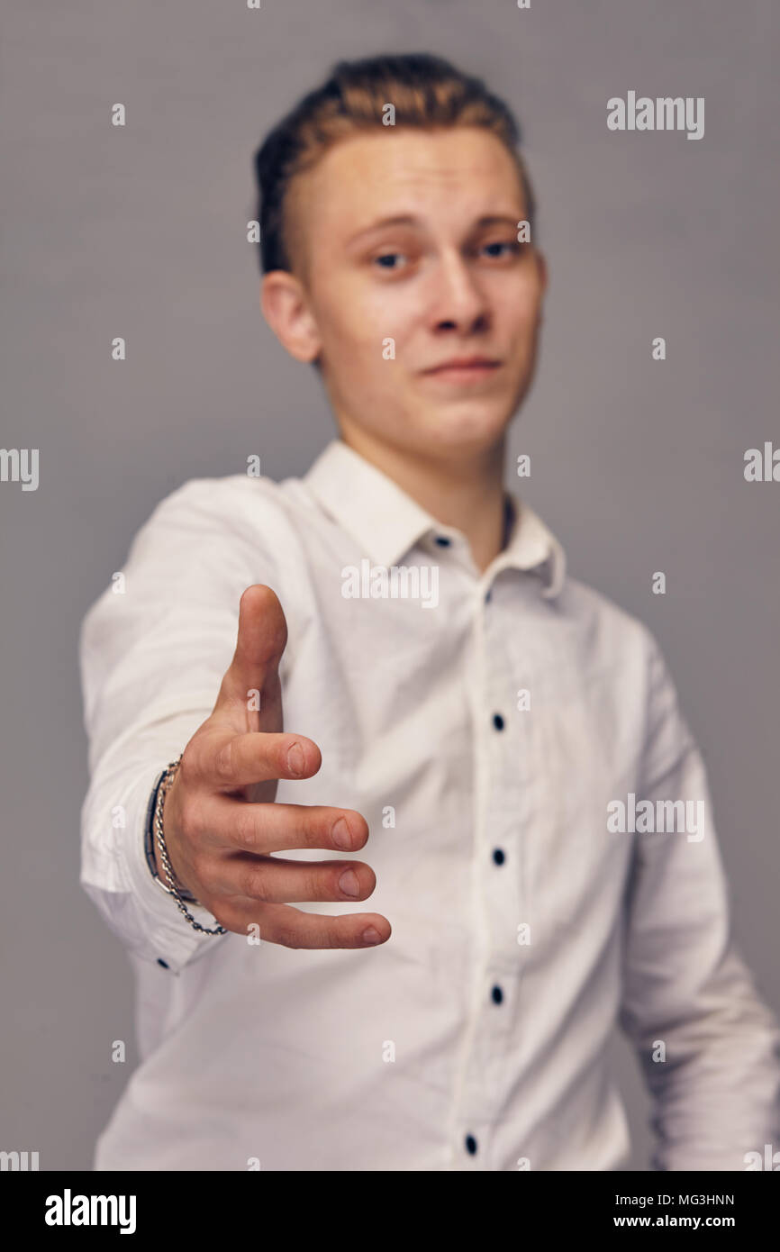 Un giovane uomo stende la mano, che mostra i suoi saluti. Ritratto in studio contro uno sfondo grigio Foto Stock