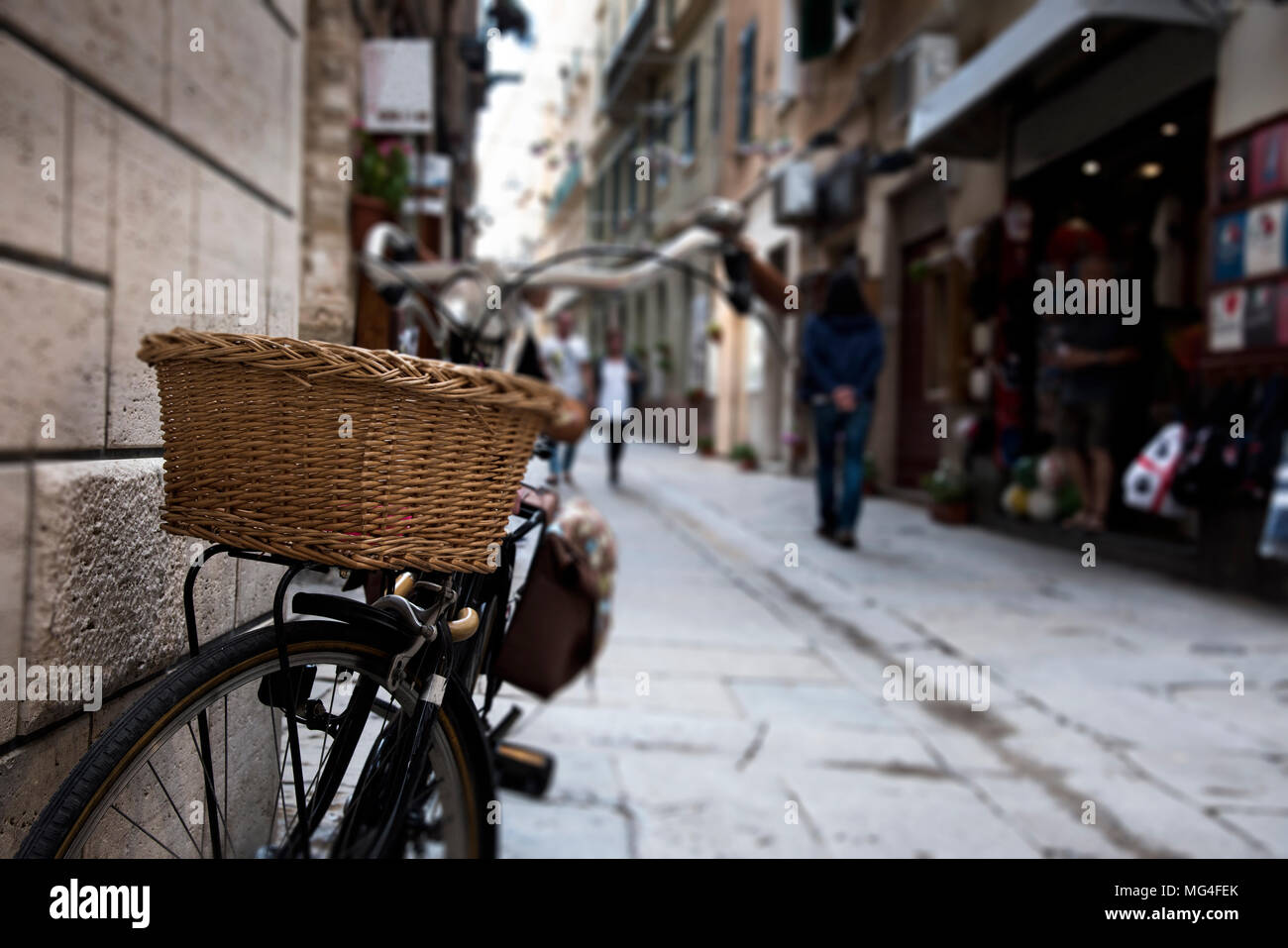 Una strada pedonale nel centro storico di Alghero, Sardegna, Italia, con una vecchia bicicletta parcheggiata in una parete in primo piano Foto Stock