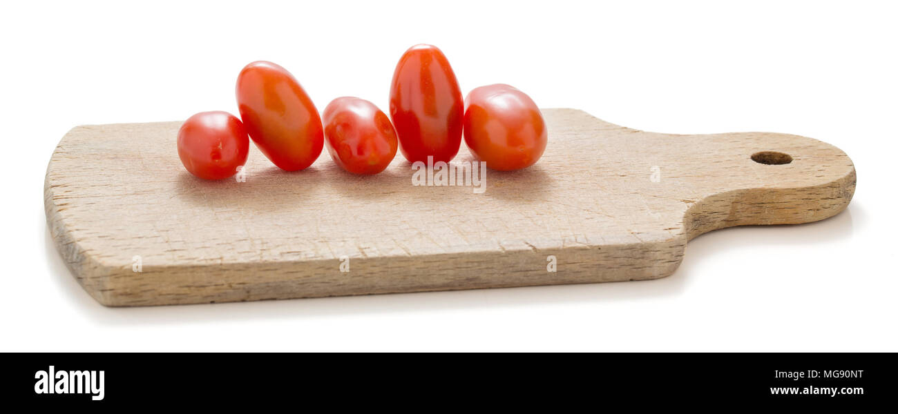 Pomodori di piccole dimensioni su un tagliere di legno su sfondo bianco Foto Stock