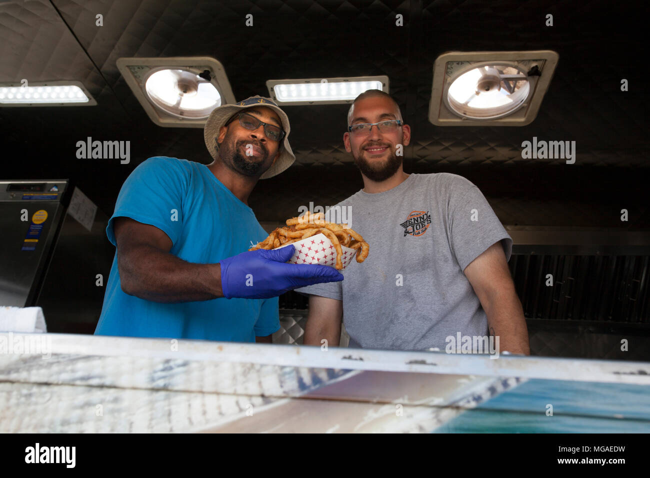 Afro-americano e Caucasico i proprietari di piccole imprese nella loro alimentazione carrello con un basketful di anelli di cipolla fritti Foto Stock