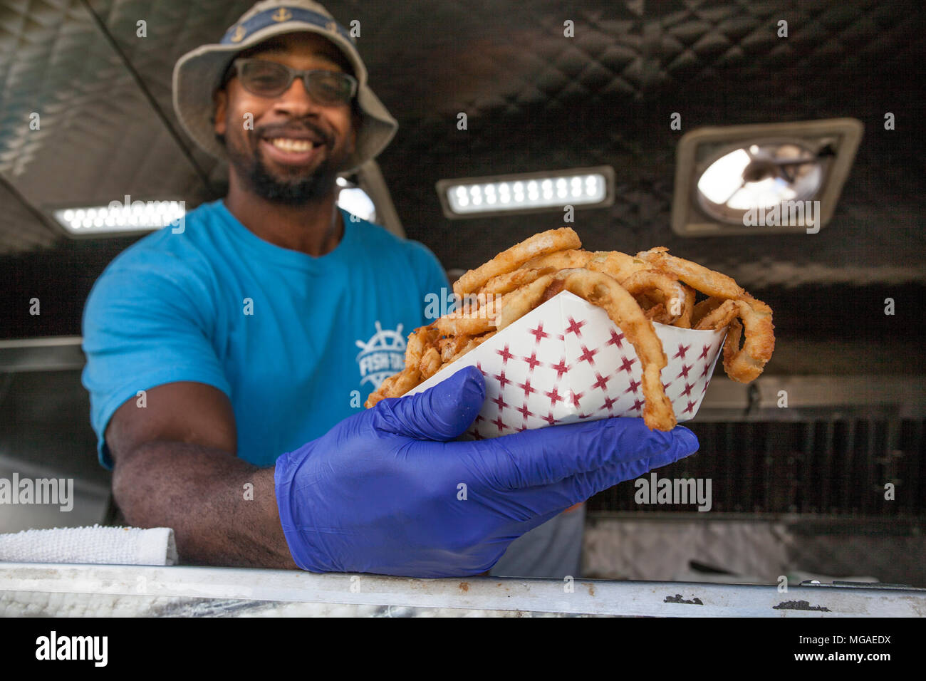 Ritratto di un afro-americano di proprietario di piccola impresa nel suo cibo carrello con un cesto pieno di anelli di cipolla fritti Foto Stock