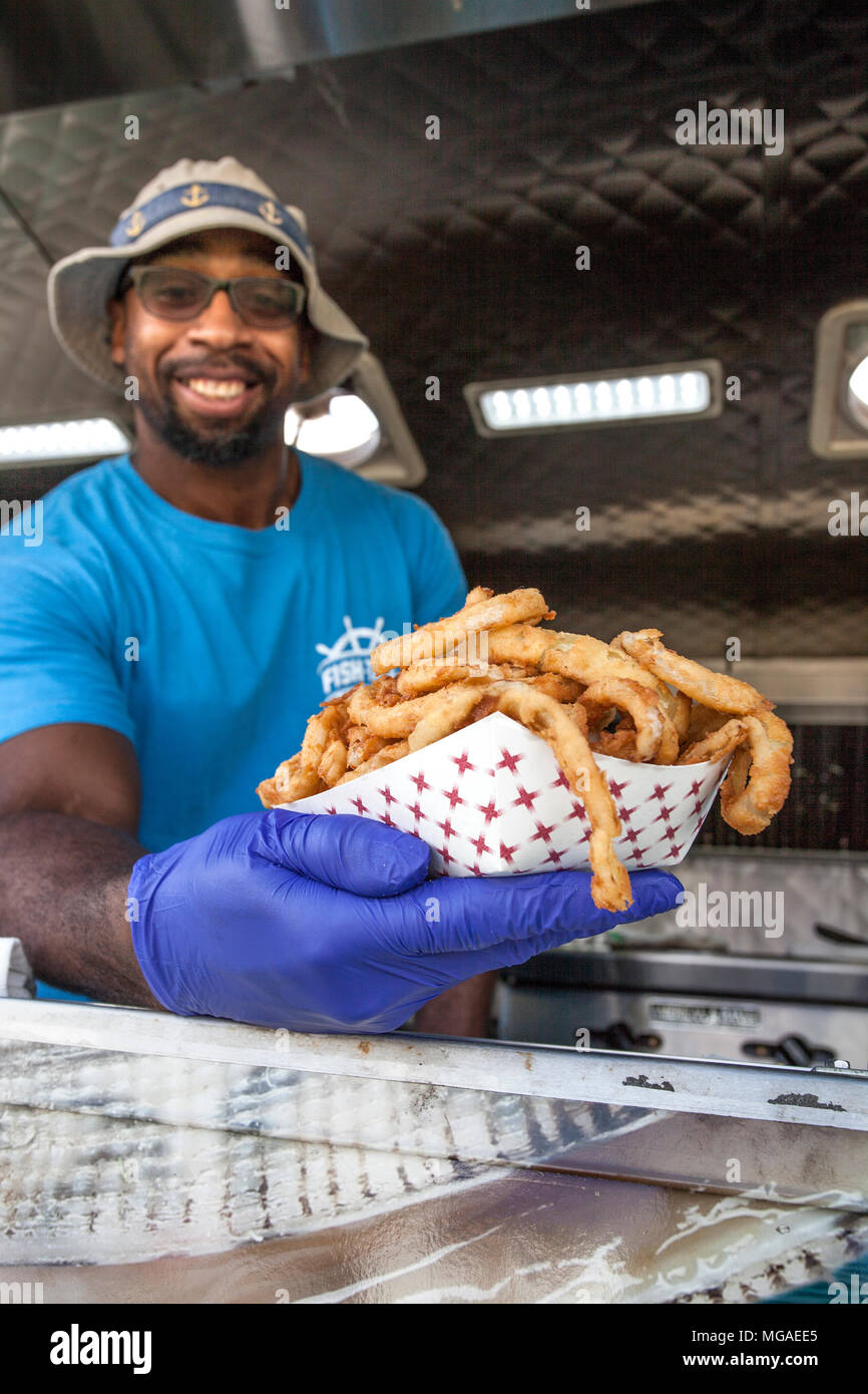 Ritratto di un afro-americano di proprietario di piccola impresa nel suo cibo carrello con un cesto pieno di anelli di cipolla fritti Foto Stock