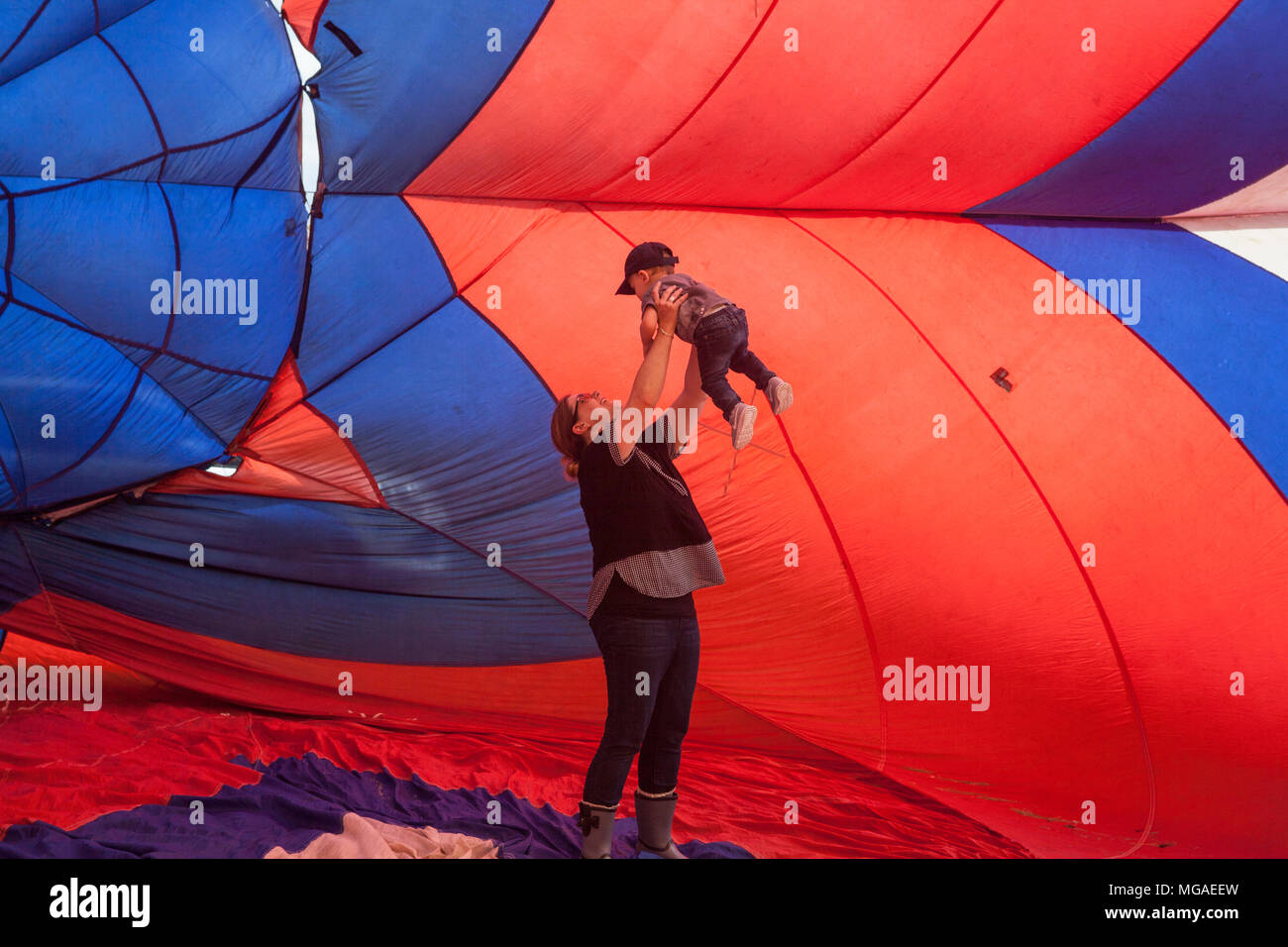 Allegro mom sollevando il suo piacere due-anno-vecchio figlio all'interno di una soffiata fino in mongolfiera ad aria calda in un balloon festival Foto Stock