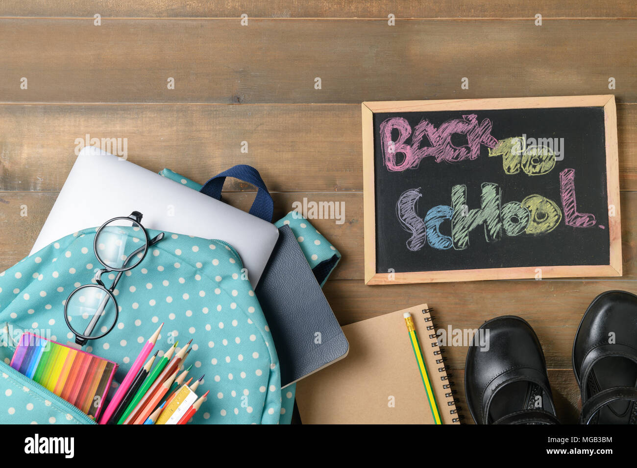 Si torna a scuola il testo su gesso nero bordo con sacco e forniture scolastiche su uno sfondo di legno, si torna a scuola e il concetto di istruzione Foto Stock