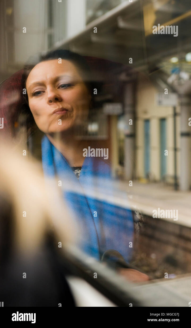 Donna seduta sul treno, guardando fuori della finestra, la sua riflessione visto in vetro, contemplando Foto Stock