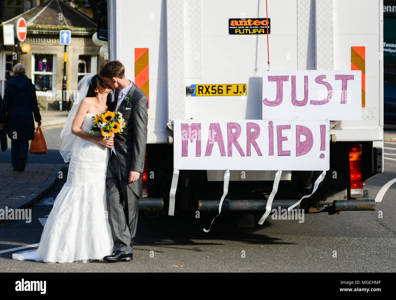 Coppia di novelli sposi kissing, accanto al carrello con grande 'Just Married " segno attaccato alla parte posteriore Foto Stock