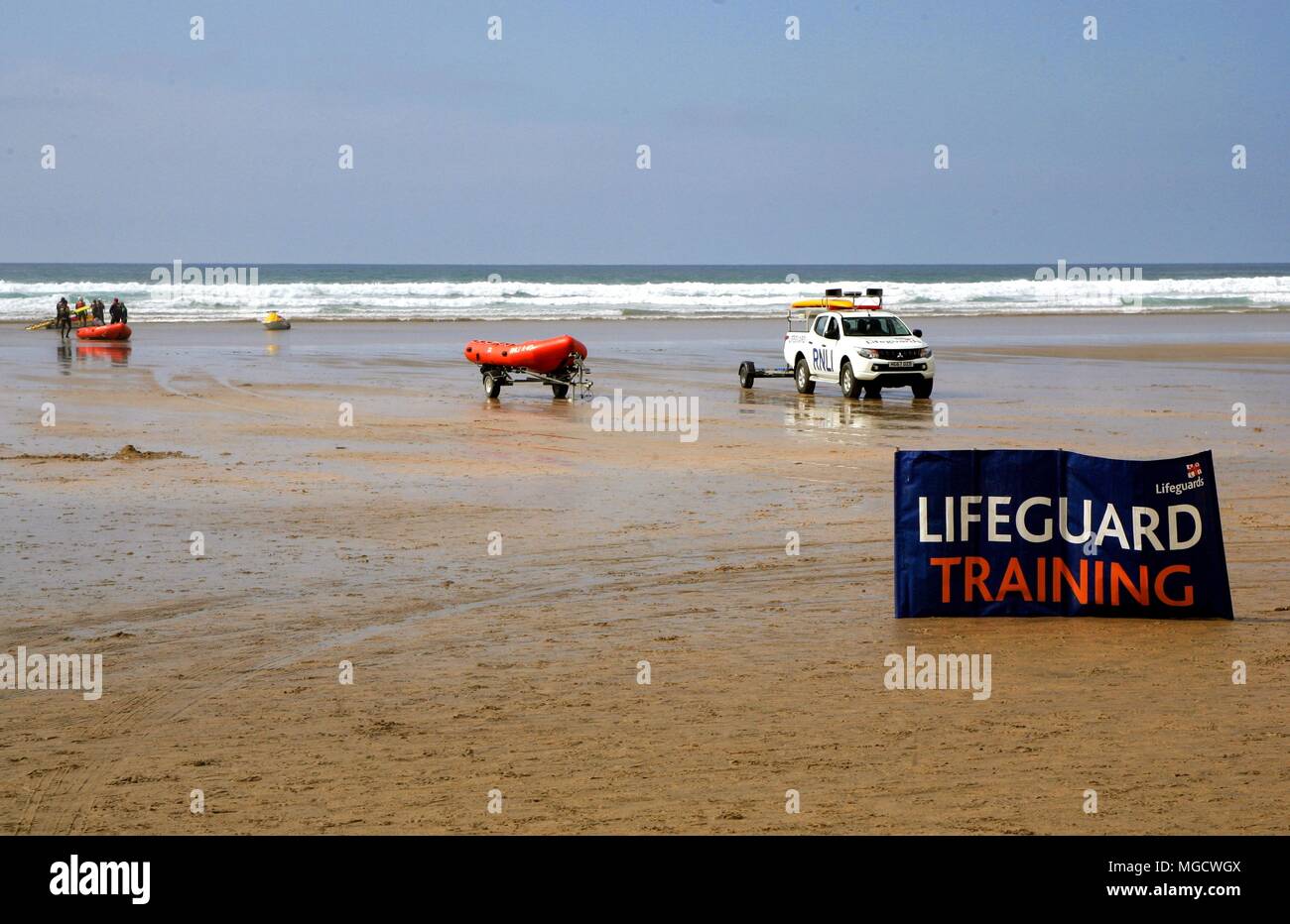 Perranporth, Cornwall, Regno Unito - 9 Aprile 2018: RNLI bagnini di formazione in surf su una spiaggia, con carrello, derive e idrogetti, dietro un grande segno. Foto Stock