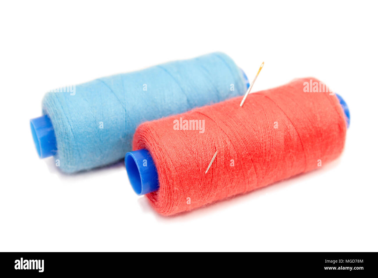 Bobine di filo per cucire di blu e rosso con loro bloccato in un ago di cucitura isolati su sfondo bianco. Foto Stock