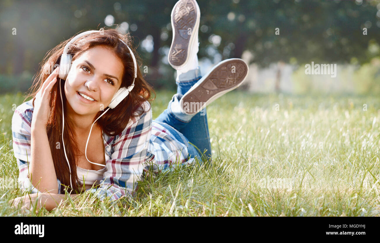 Ritratto di giovane ragazza ascoltando musica giacente in corrispondenza dell'erba. Carino ragazza adolescente relax nel parco Foto Stock