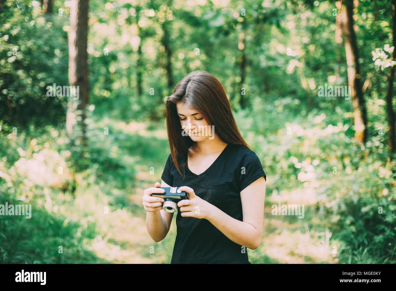 I Capelli rossi ragazza caucasica donna giovane fotografo fotografare il vecchio Retro Vintage fotocamera a pellicola in estate foresta verde. Ragazza vestita di un Nero T Foto Stock