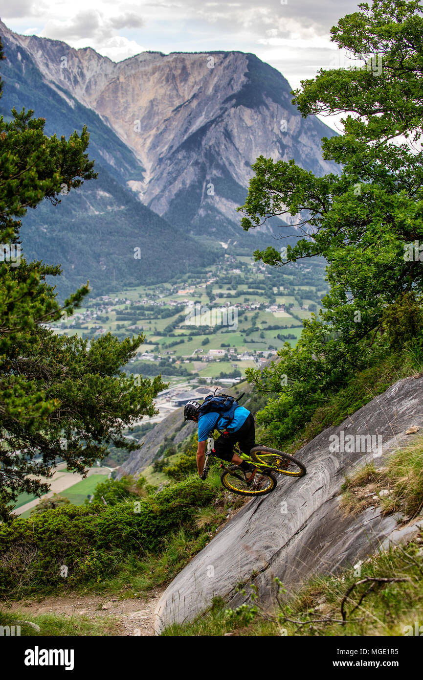 Un uomo corse in mountain bike in alto sopra il piano della valle in prossimità della città di Gampel e Jeizinen in Vallese della Svizzera. Foto Stock
