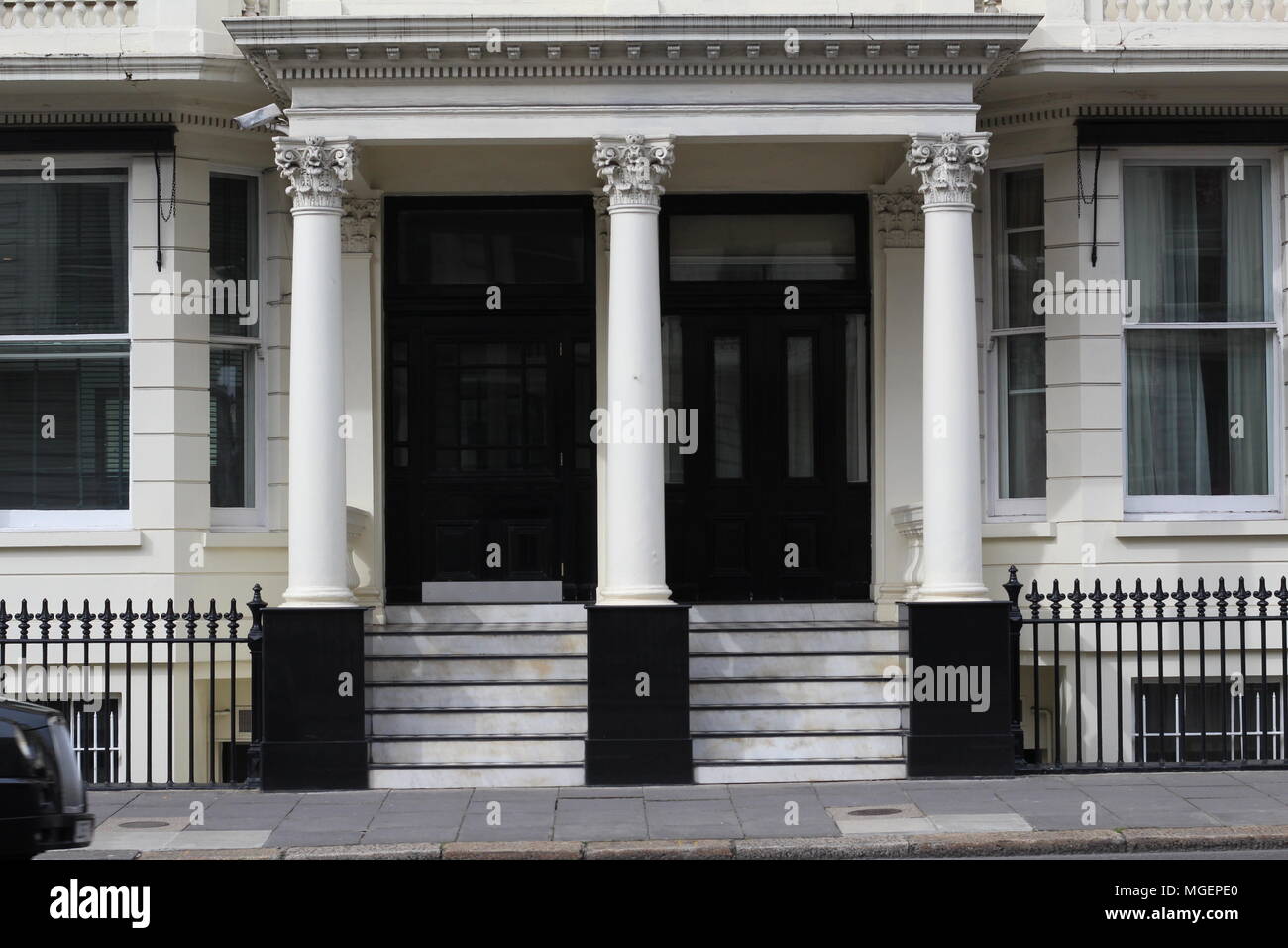 Entrata privata di un edificio londinese con tre colonne bianche e una rampa di scale che portano alle porte nero creando un forte contrasto Foto Stock