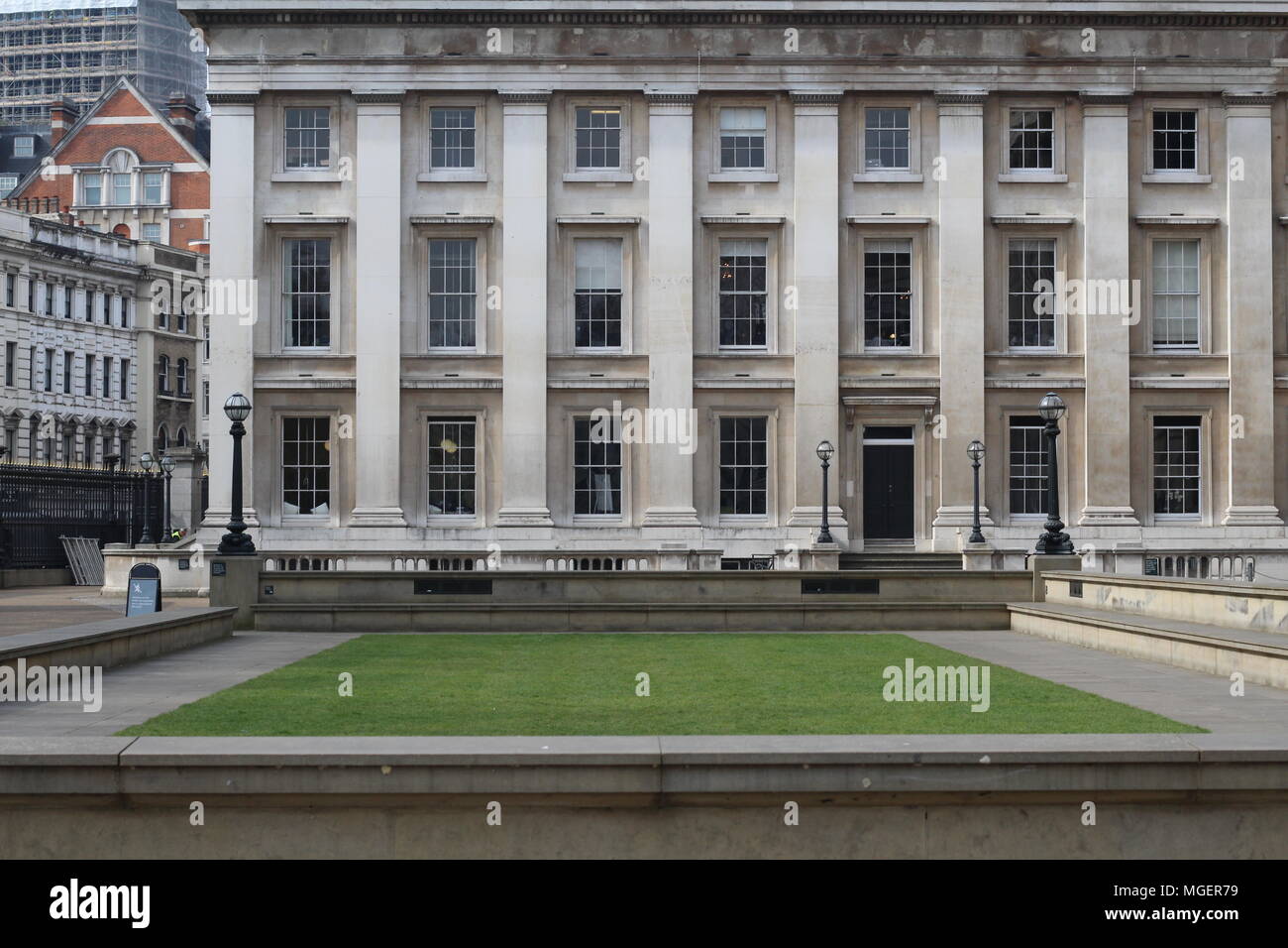 Simmetrie creata tra un edificio con grandi finestre e una piazza di fronte al palazzo con un quadrato verde Foto Stock